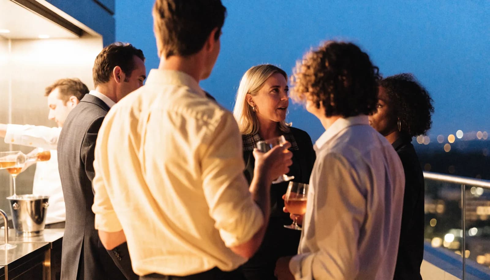 Residents in conversation at a rooftop tasting evening at dusk.